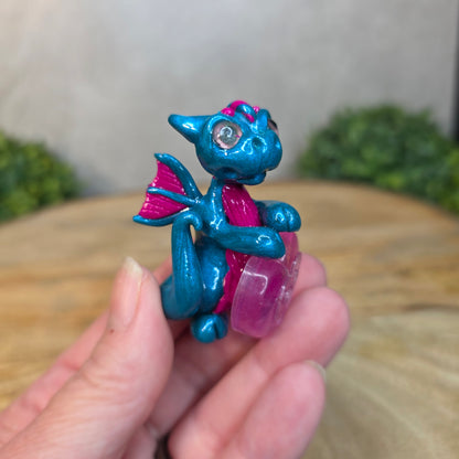 Hand holding a blue and pink clay dragon with a blurred background