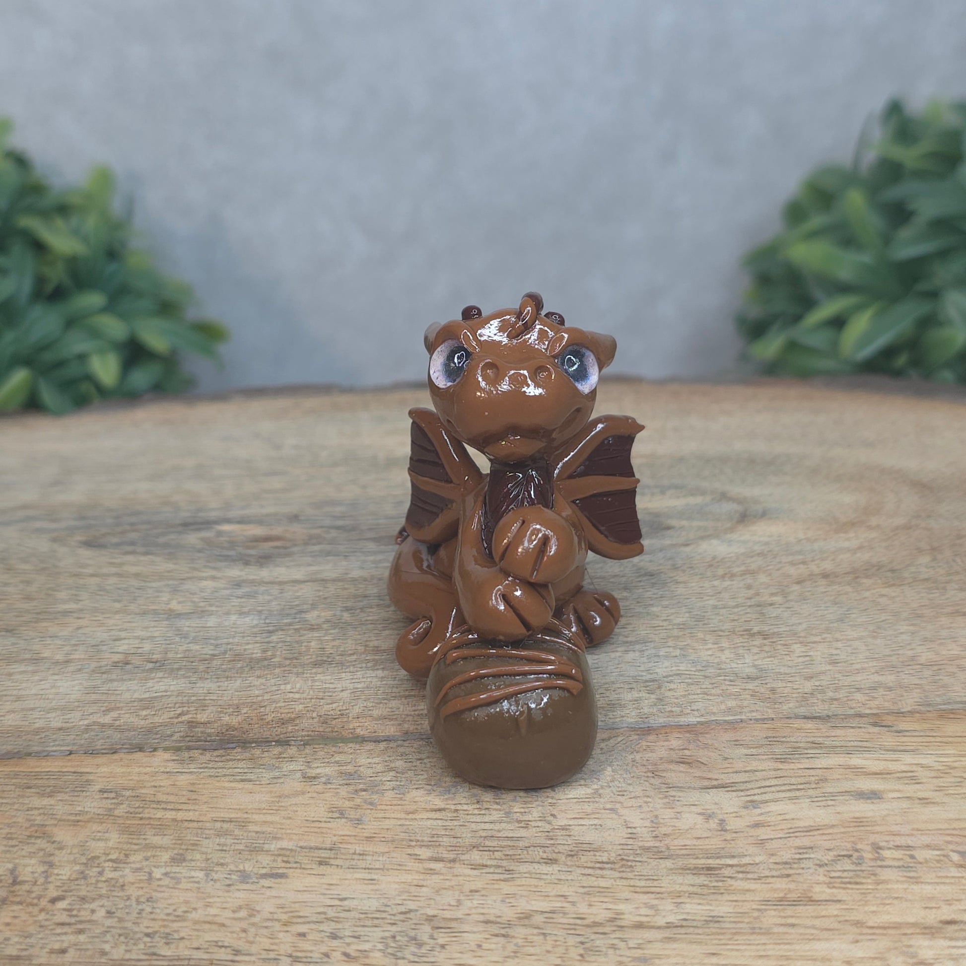 A baby polymer clay dragon with a chocolate truffle against a blurred background