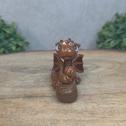 A baby polymer clay dragon with a chocolate truffle against a blurred background