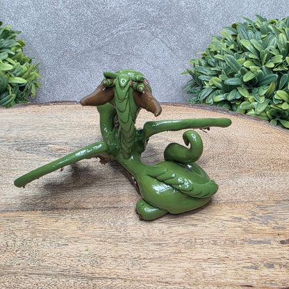 Back view of a clay dragon with a tigers eye crystal skull against a wood surface with greenery.