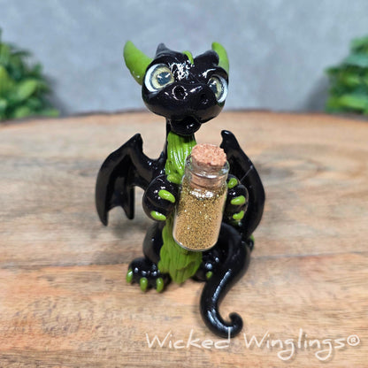 A clay dragon with a potion bottle on a wood surface. Text reads Wicked Winglings.