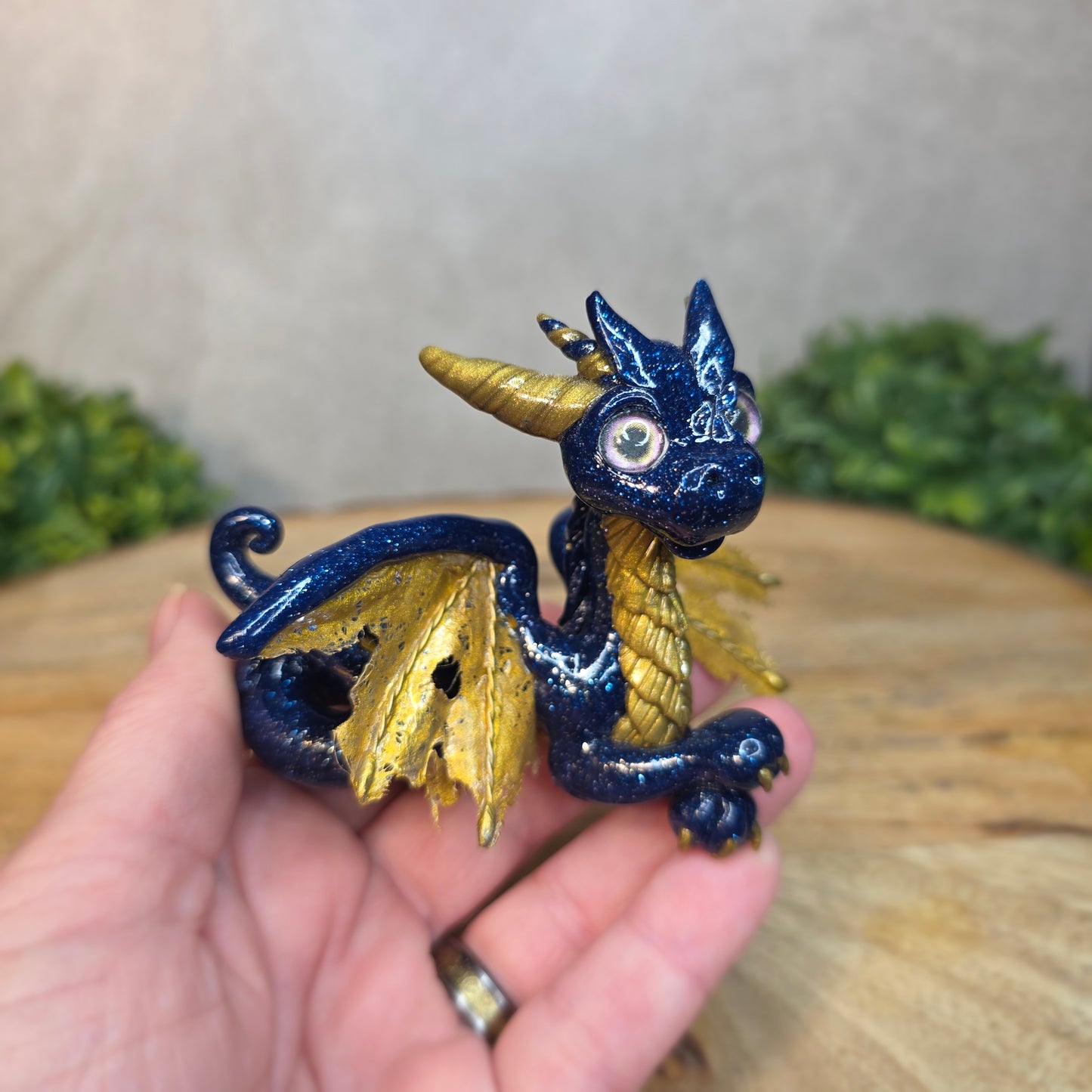 A hand holding a blue and gold clay dragon against a blurred wood surface