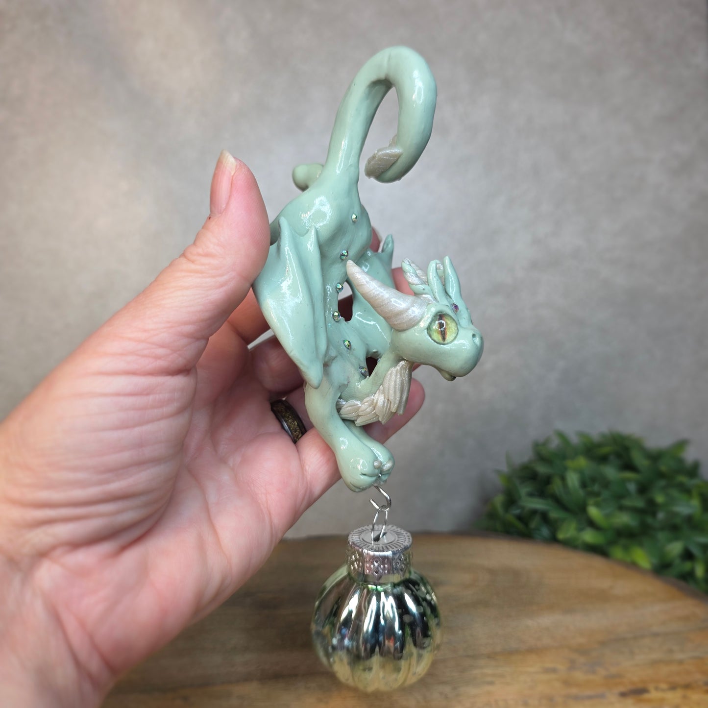 Hand holding a small aqua dragon with glass ornament against a blurred background