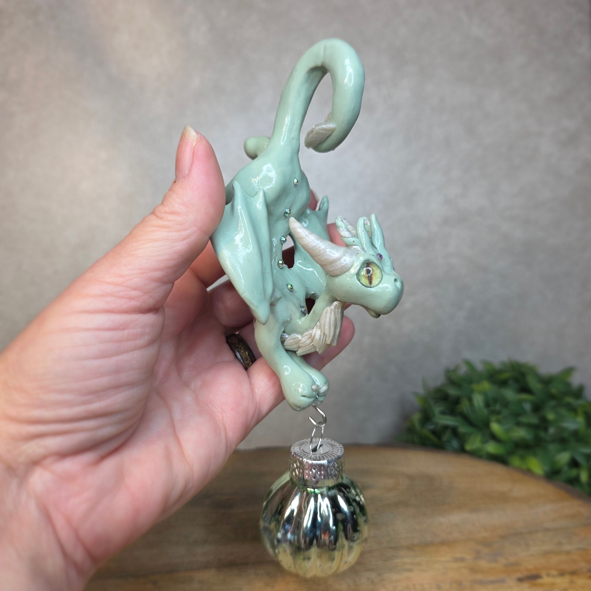 Hand holding a small aqua dragon with glass ornament against a blurred background