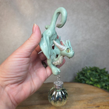 Hand holding a small aqua dragon with glass ornament against a blurred background