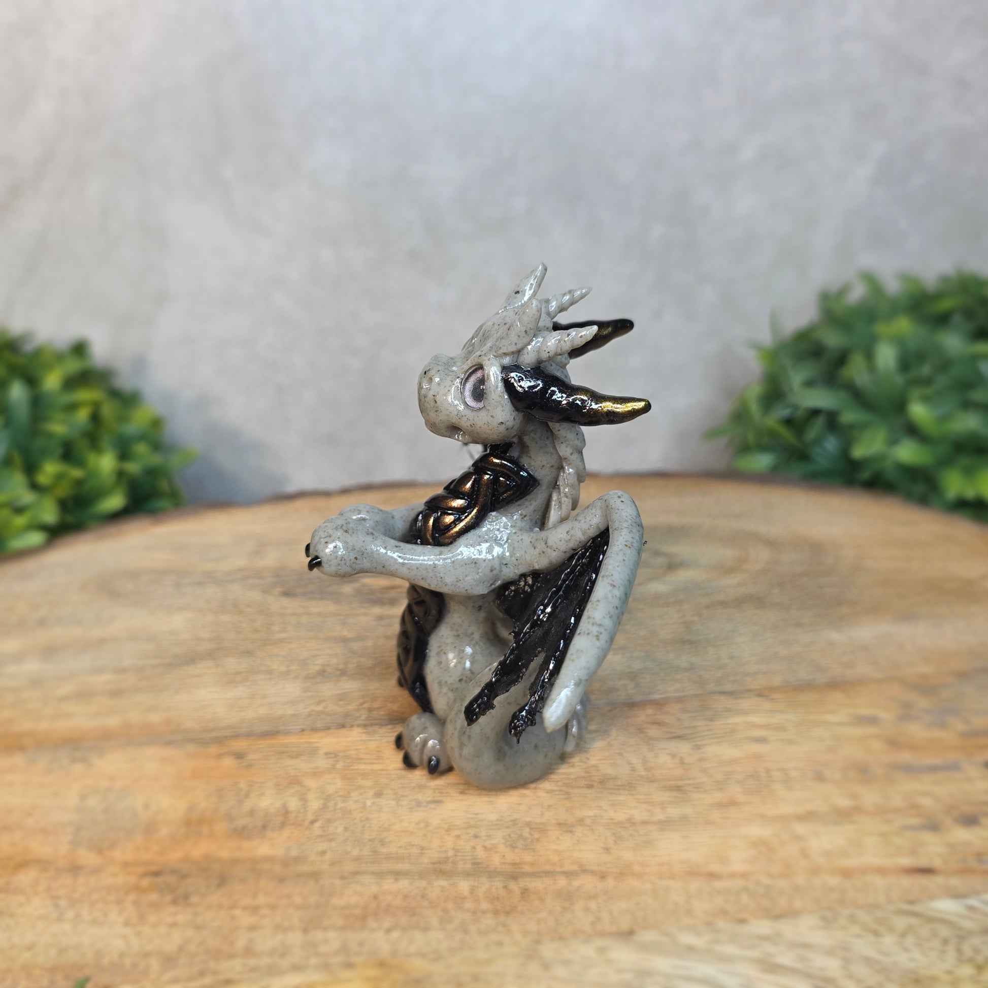 A clay dragon figurine on a wooden surface with a blurred green plant in the background