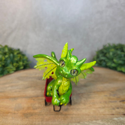 A green clay dragon in a red wagon on a wood surface