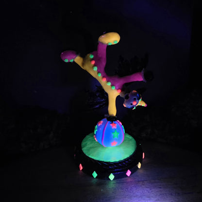 A blacklight reactive clown dragon balancing on a ball on a wood surface with greenery