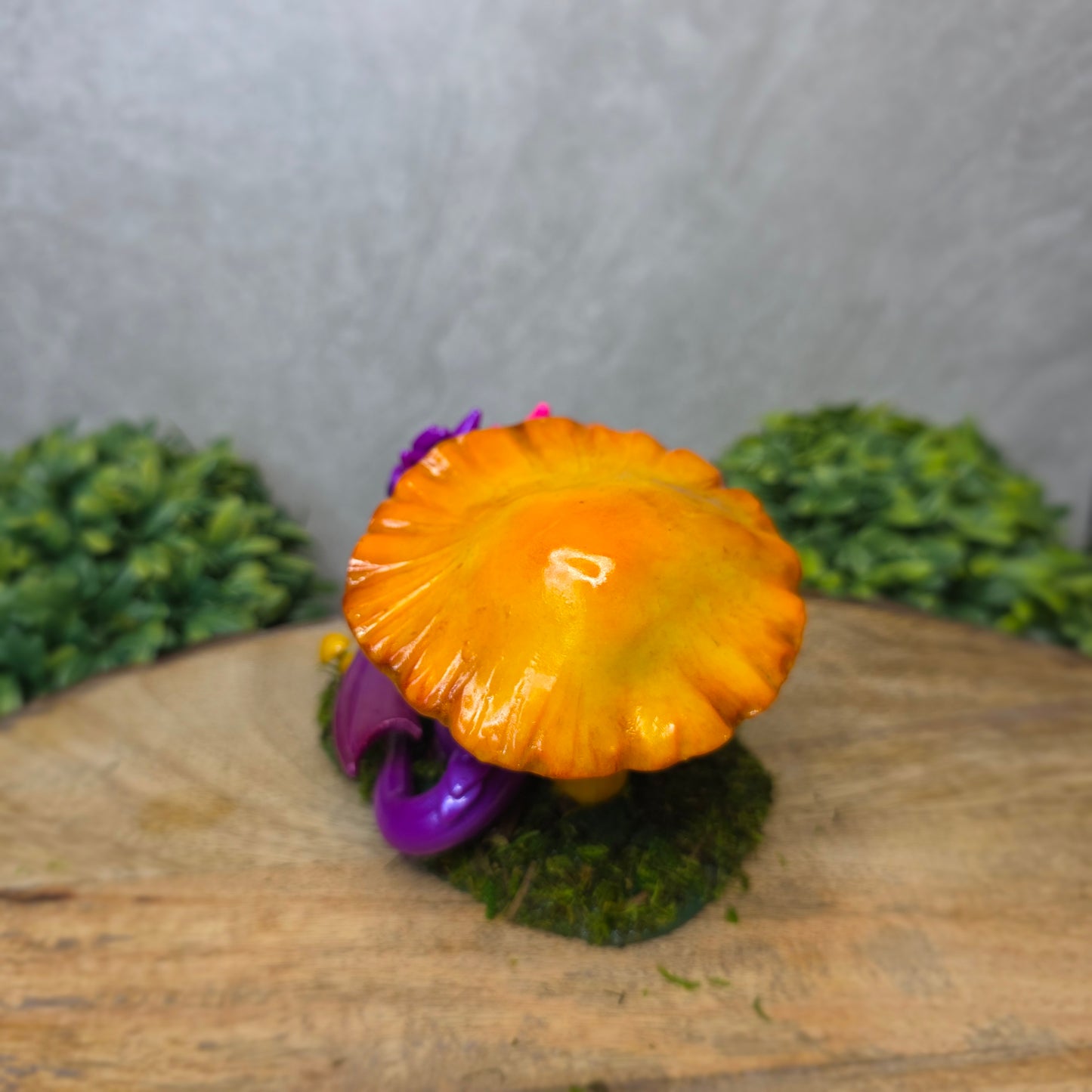 Purple dragon figurine with a yellow mushroom on a wooden surface with greenery