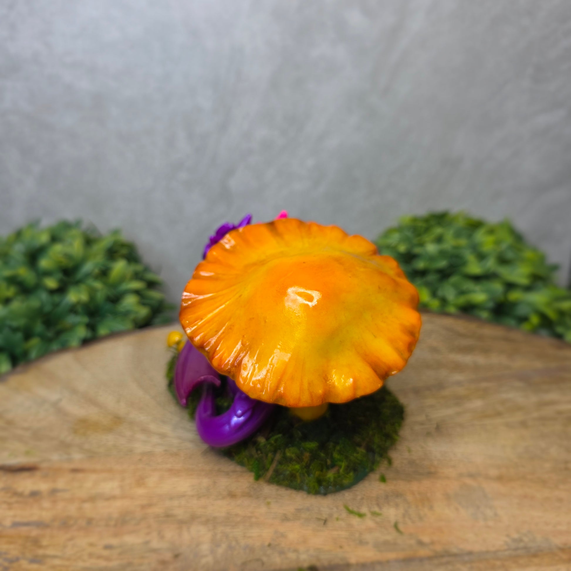Purple dragon figurine with a yellow mushroom on a wooden surface with greenery
