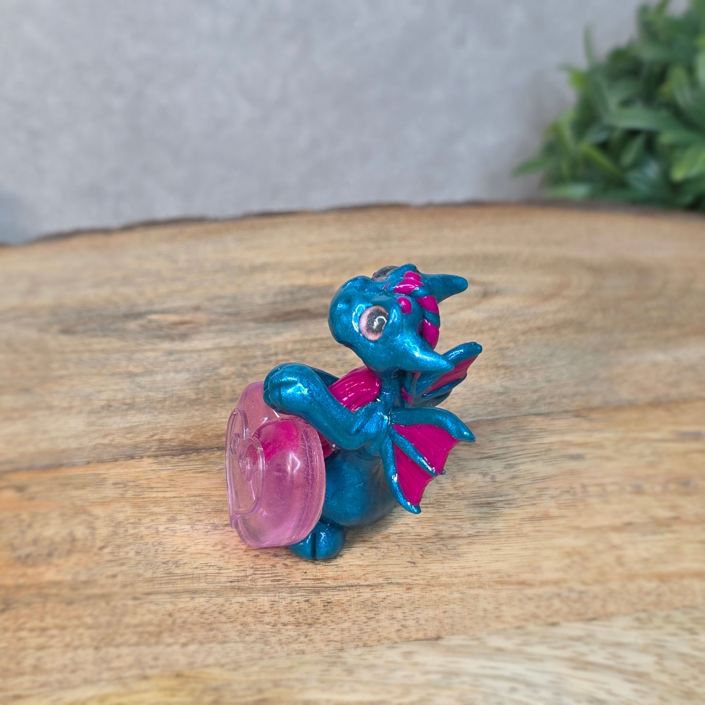 Hand holding a blue and pink clay dragon with a blurred background