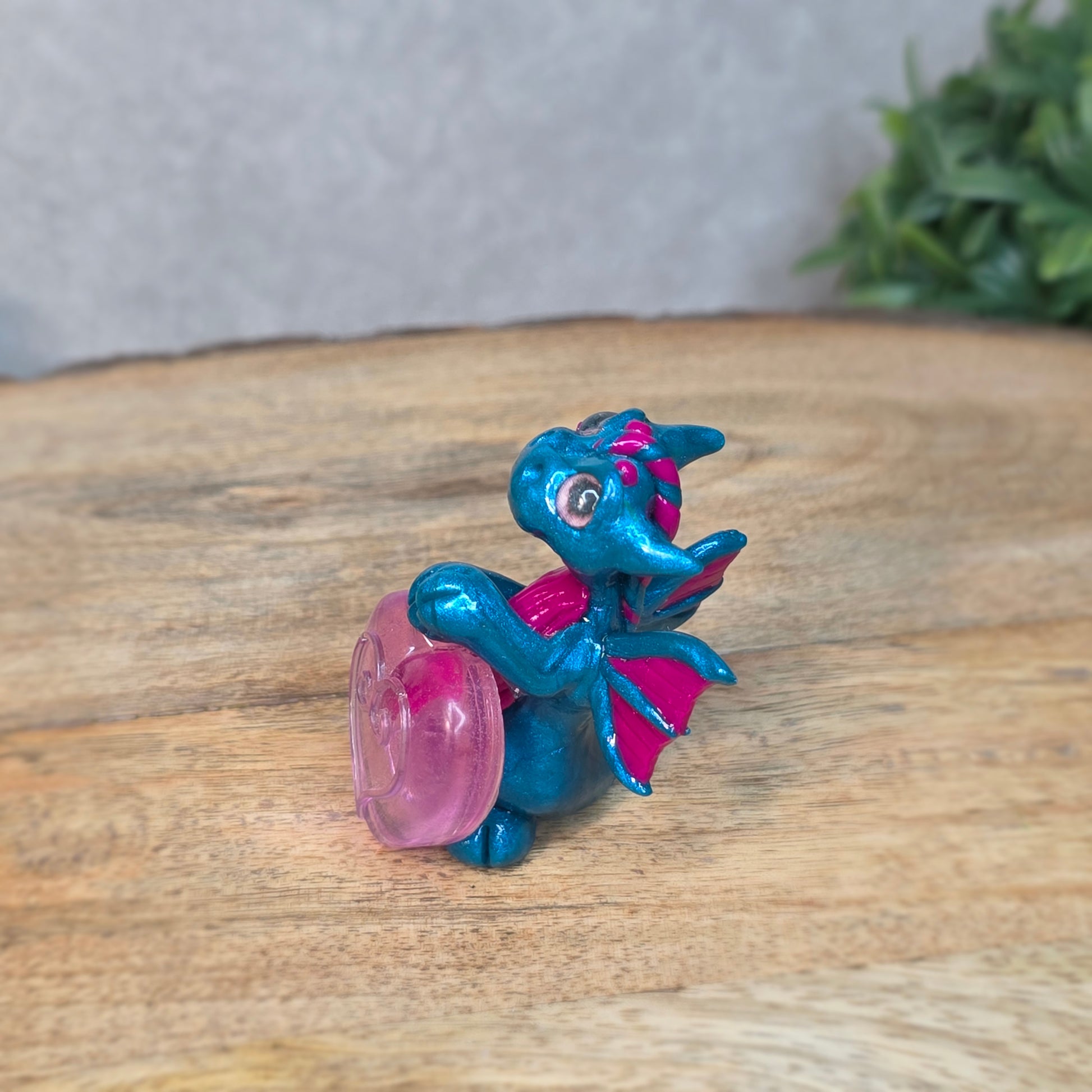 Hand holding a blue and pink clay dragon with a blurred background