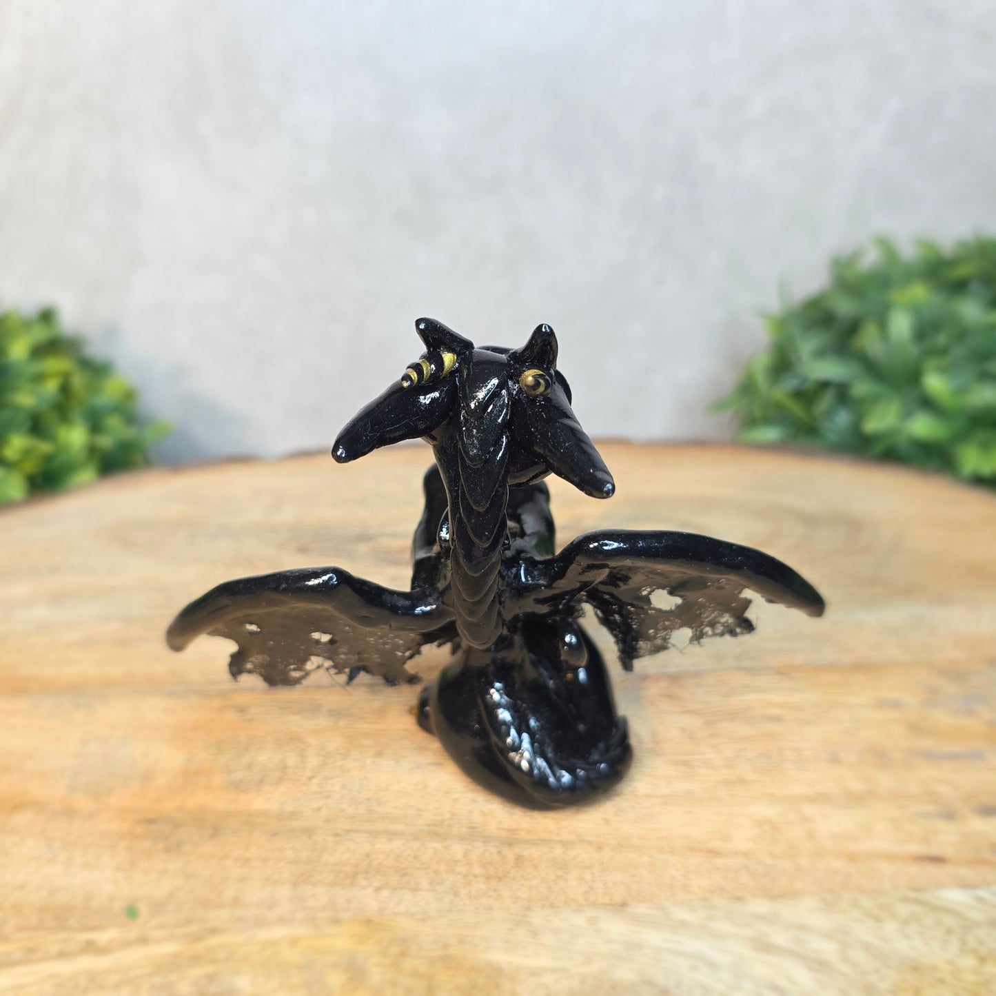 A clay dragon figurine on a wooden surface with a blurred green plant in the background