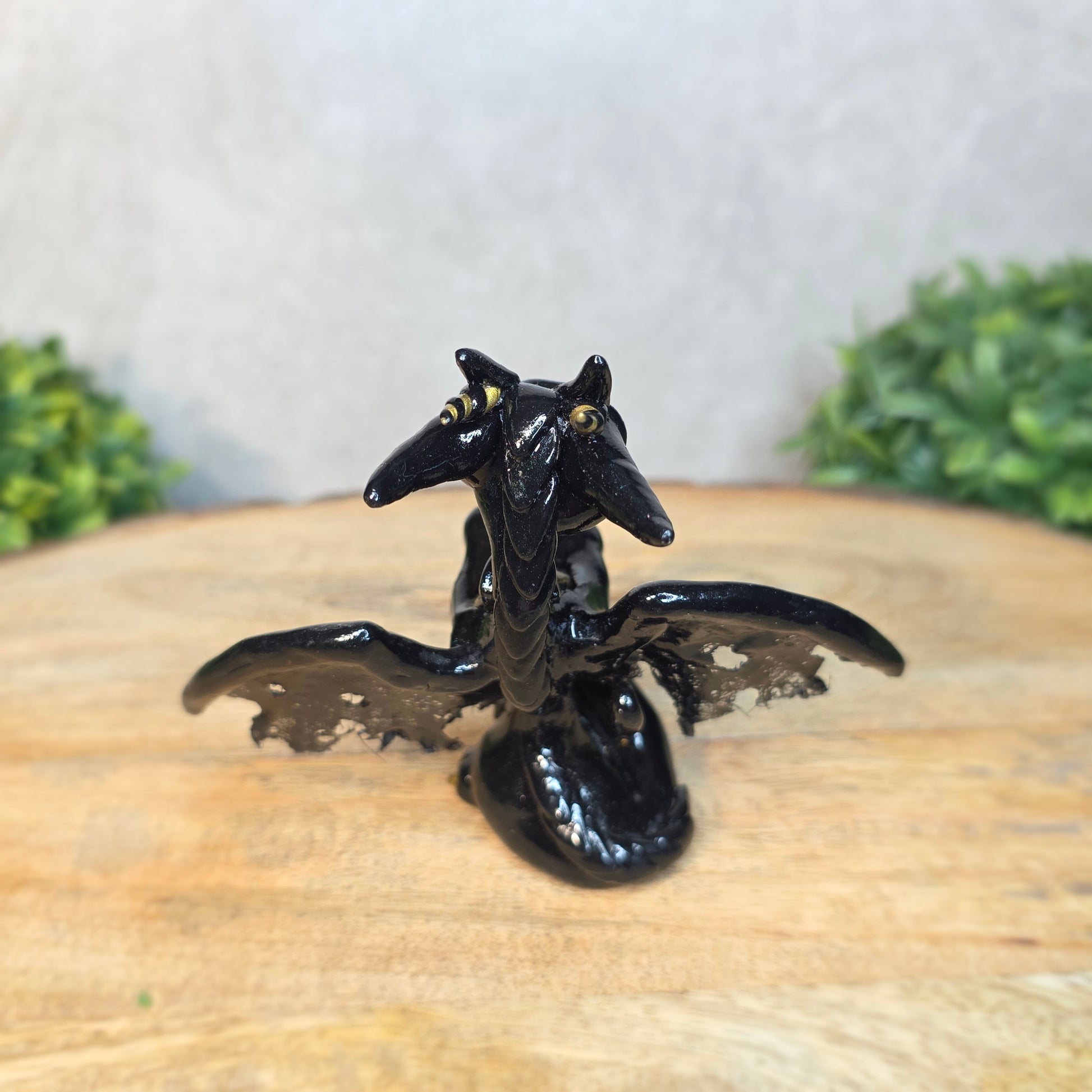 A clay dragon figurine on a wooden surface with a blurred green plant in the background