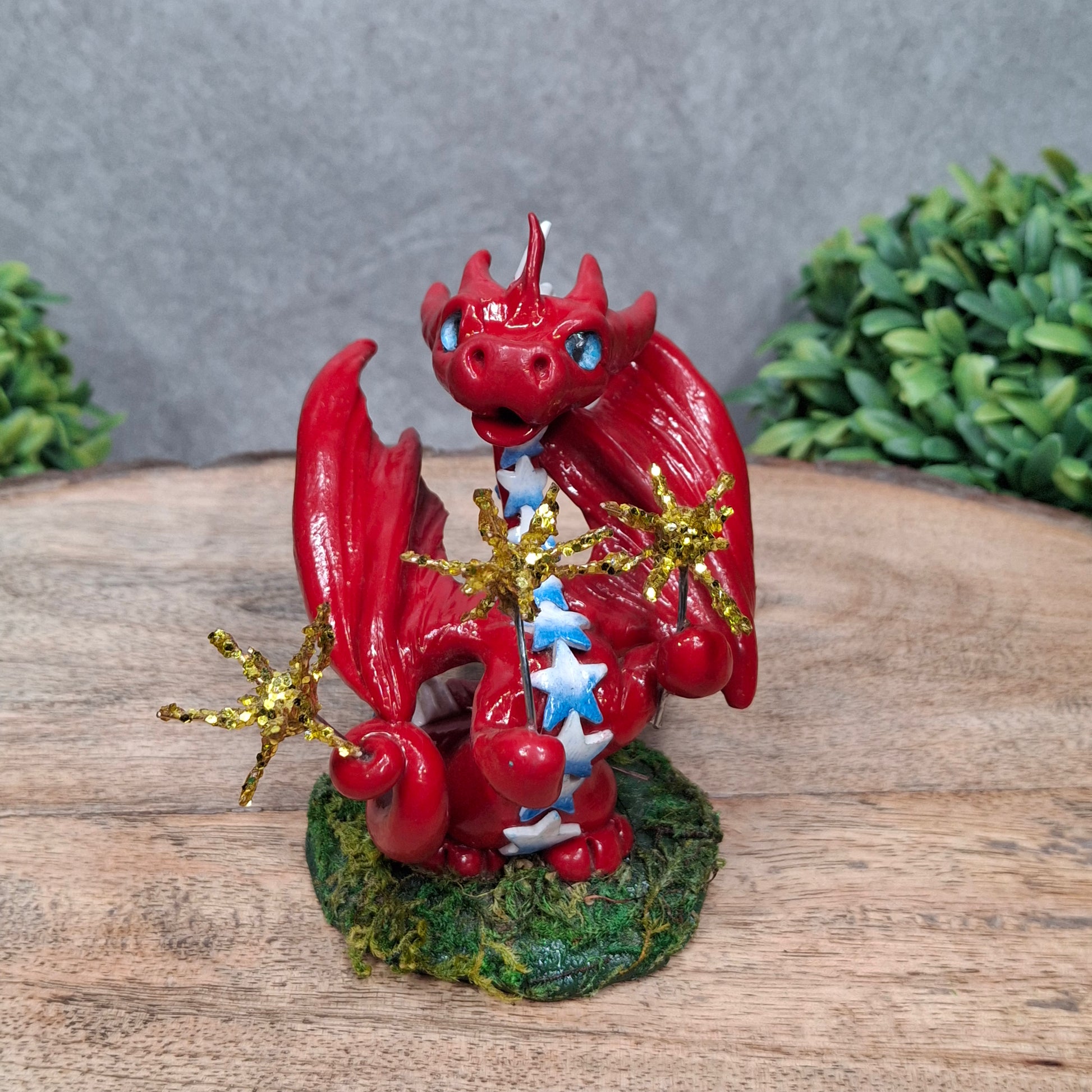 A clay dragon with sparklers against a wood surface with greenery