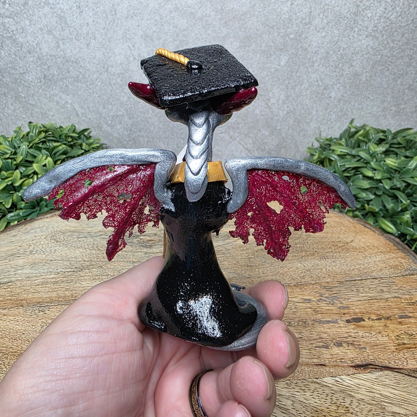 A hand holding a clay dragon in a graduation cap and gown 