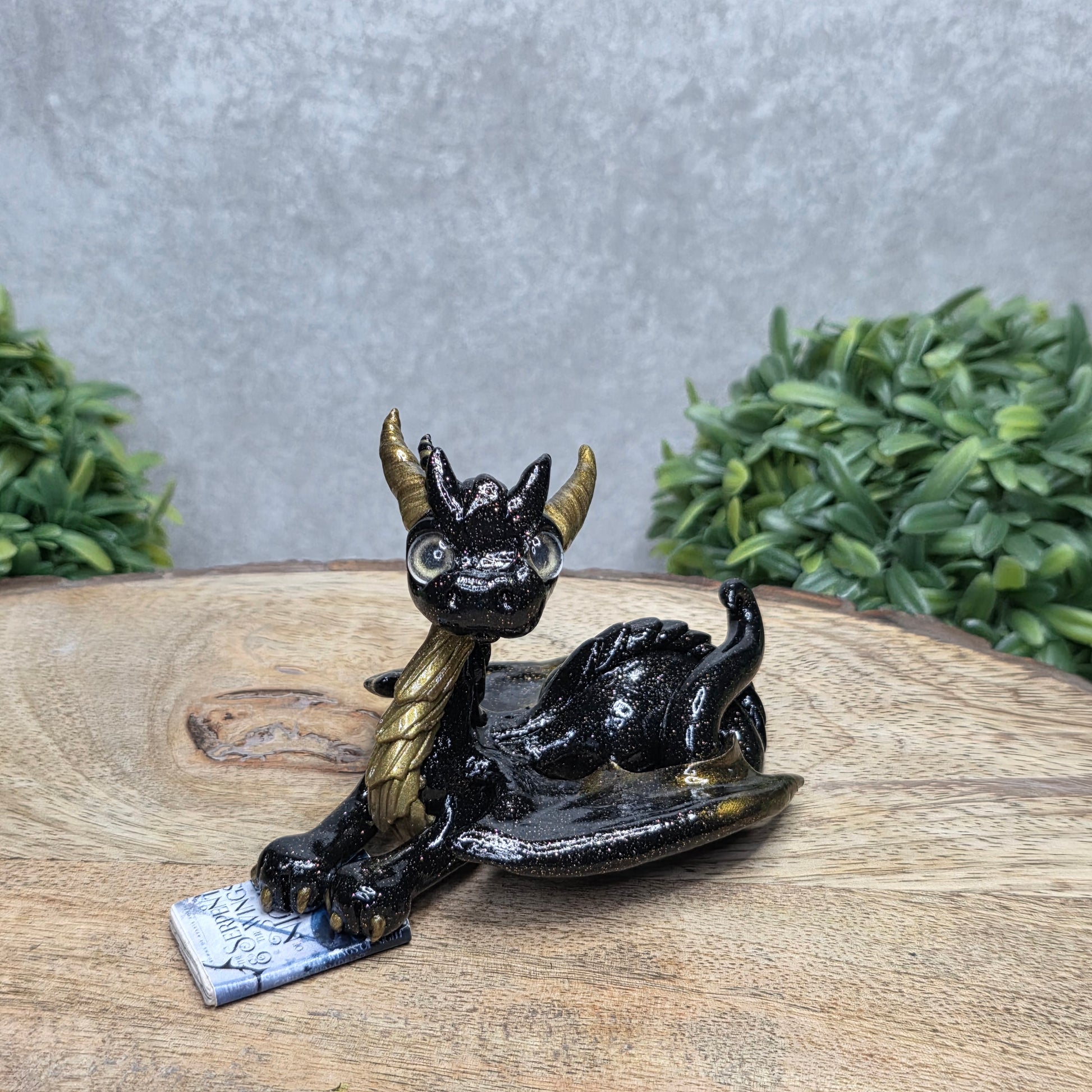A dragon reading a book against a wood surface with greenery
