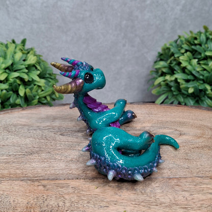 A clay dragon against a wood background with greenery