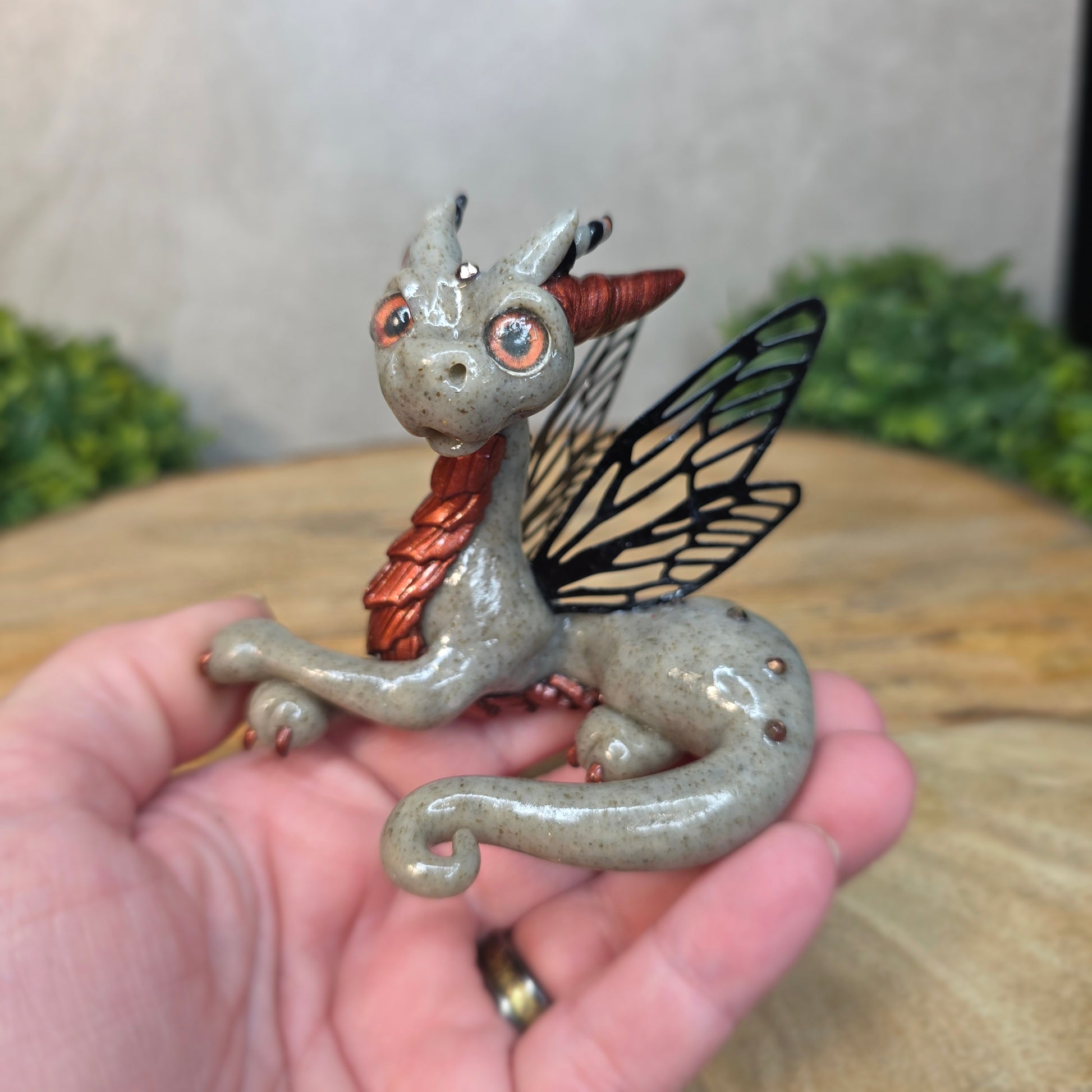 Hand holding a clay fairy dragon figurine with butterfly wings.