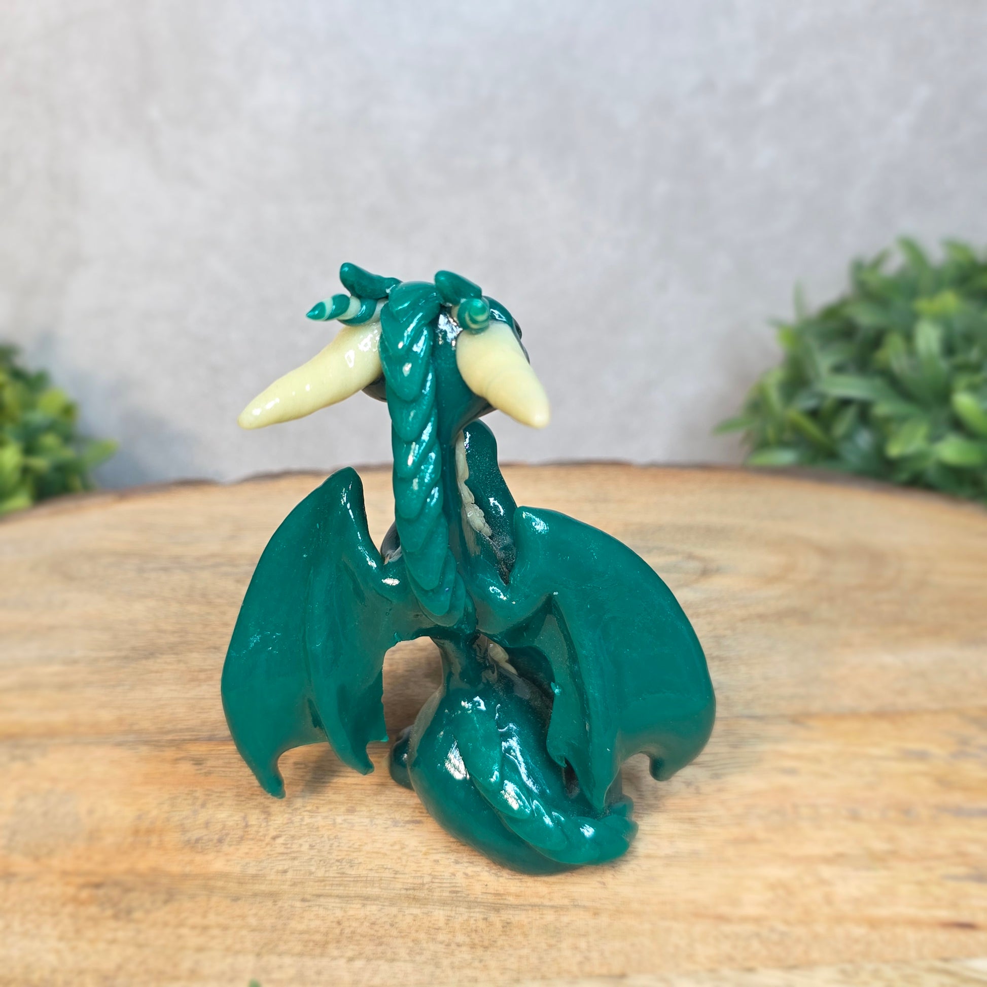 A green and cream clay dragon against a blurred wood surface
