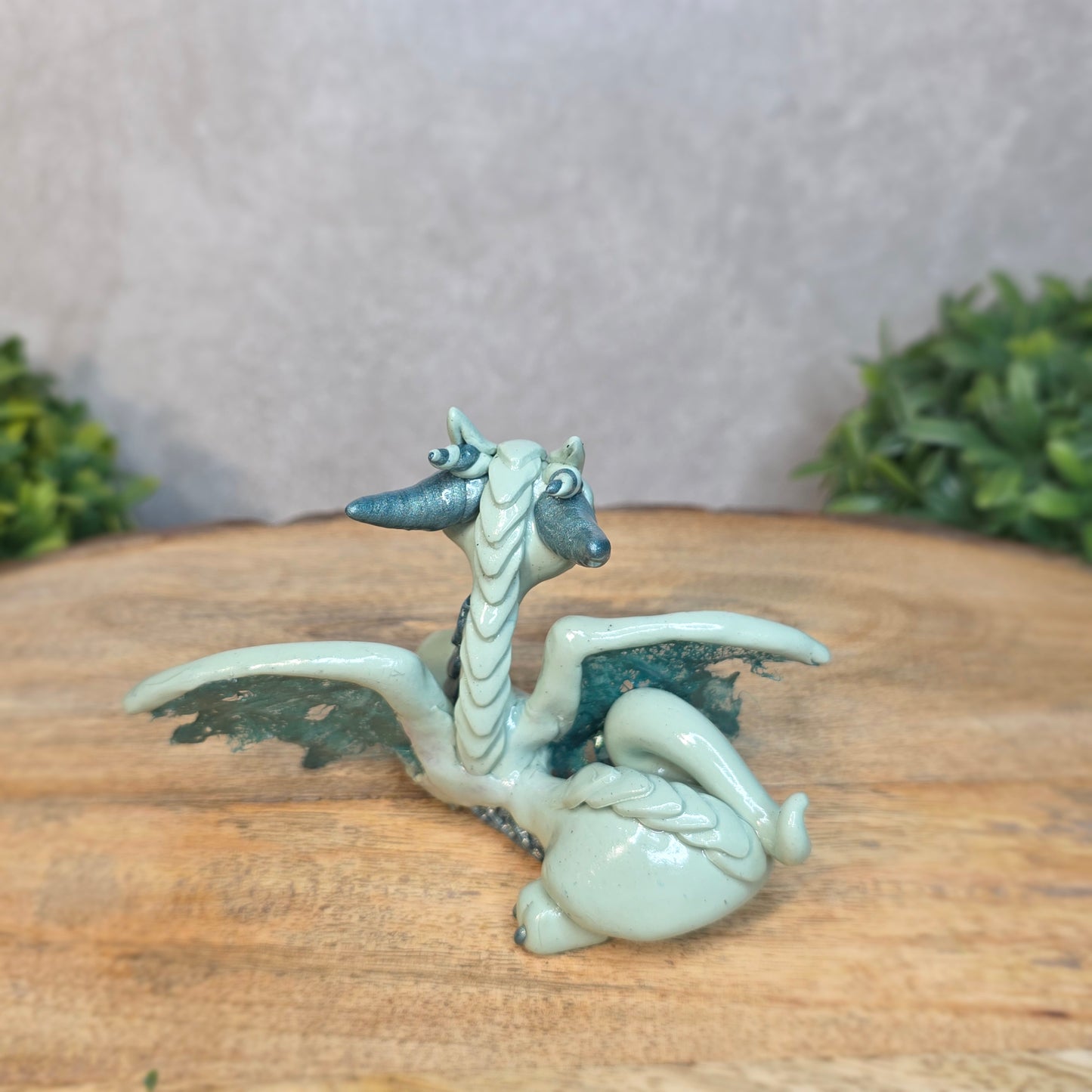 An aqua and turquoise clay dragon against a blurred wood surface