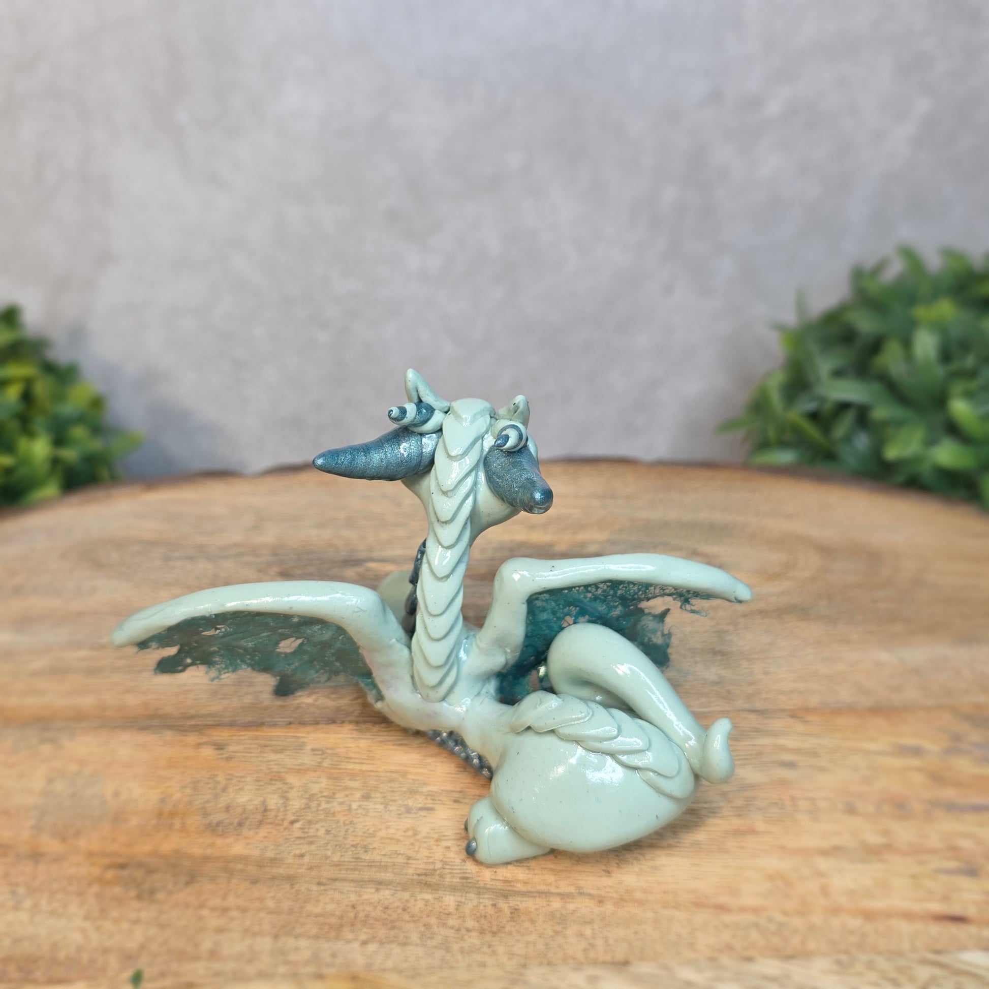An aqua and turquoise clay dragon against a blurred wood surface