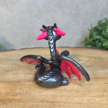 A graphite and pink clay dragon against a blurred wood surface
