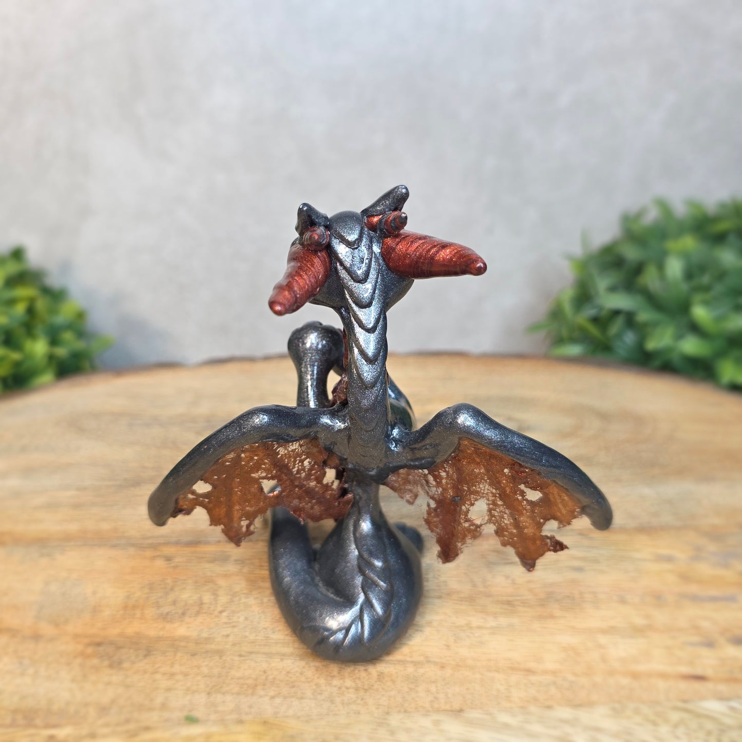 A graphite and bronze clay dragon against a blurred wood surface