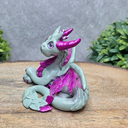 Side view of a clay dragon against a wood surface with greenery.