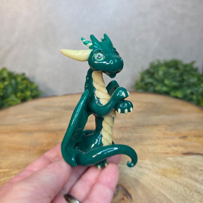 A hand holding a green and cream clay dragon against a blurred wood surface