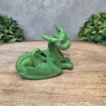 A flocked clay dragon sculpture on a wood surface with greenery.