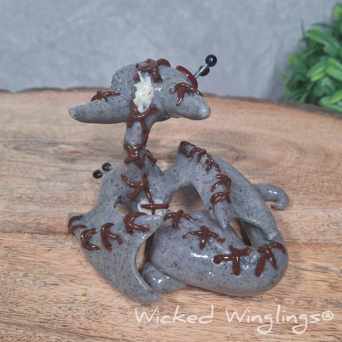 Back view of A clay voodoo dragon on a wood surface with greenery. Text says Wicked Winglings