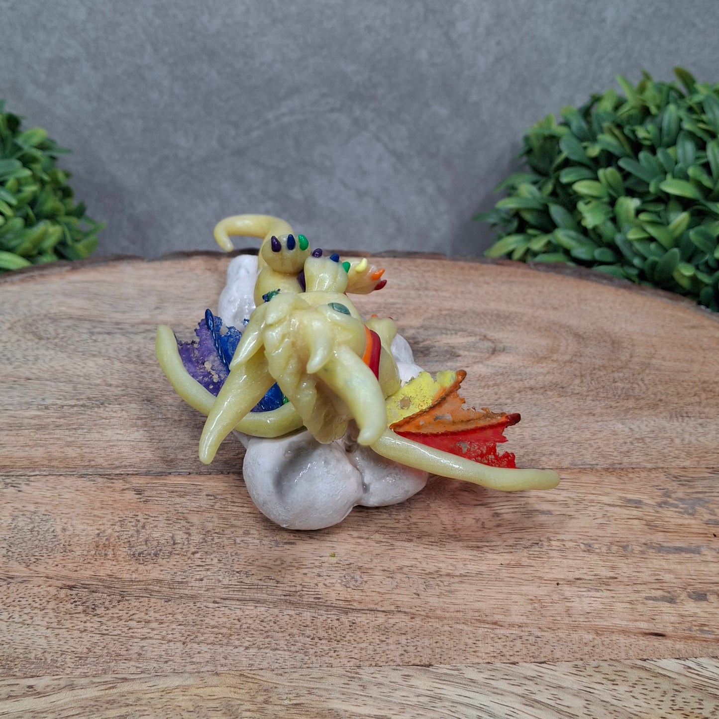 A yellow dragon with rainbow accents on a cloud sitting against a wood surface with greenery