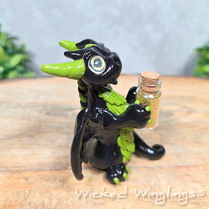 A clay dragon with a potion bottle on a wood surface. Text reads Wicked Winglings.