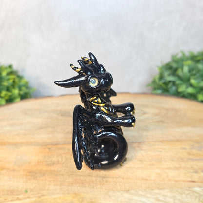 A clay dragon figurine on a wooden surface with a blurred green plant in the background