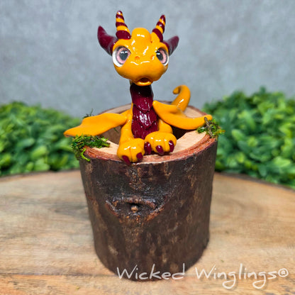 A clay dragon in a wood stump against a blurred background. Text says Wicked Winglings