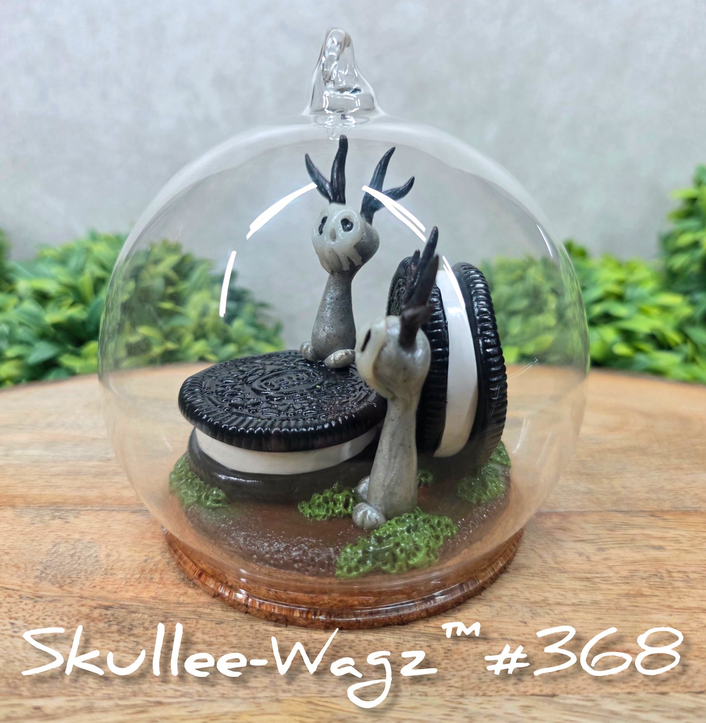 Two Skullee-Wagz with cookies in a  glass dome set on a wood surface with greenery. Text reads Skullee-Wagz #368