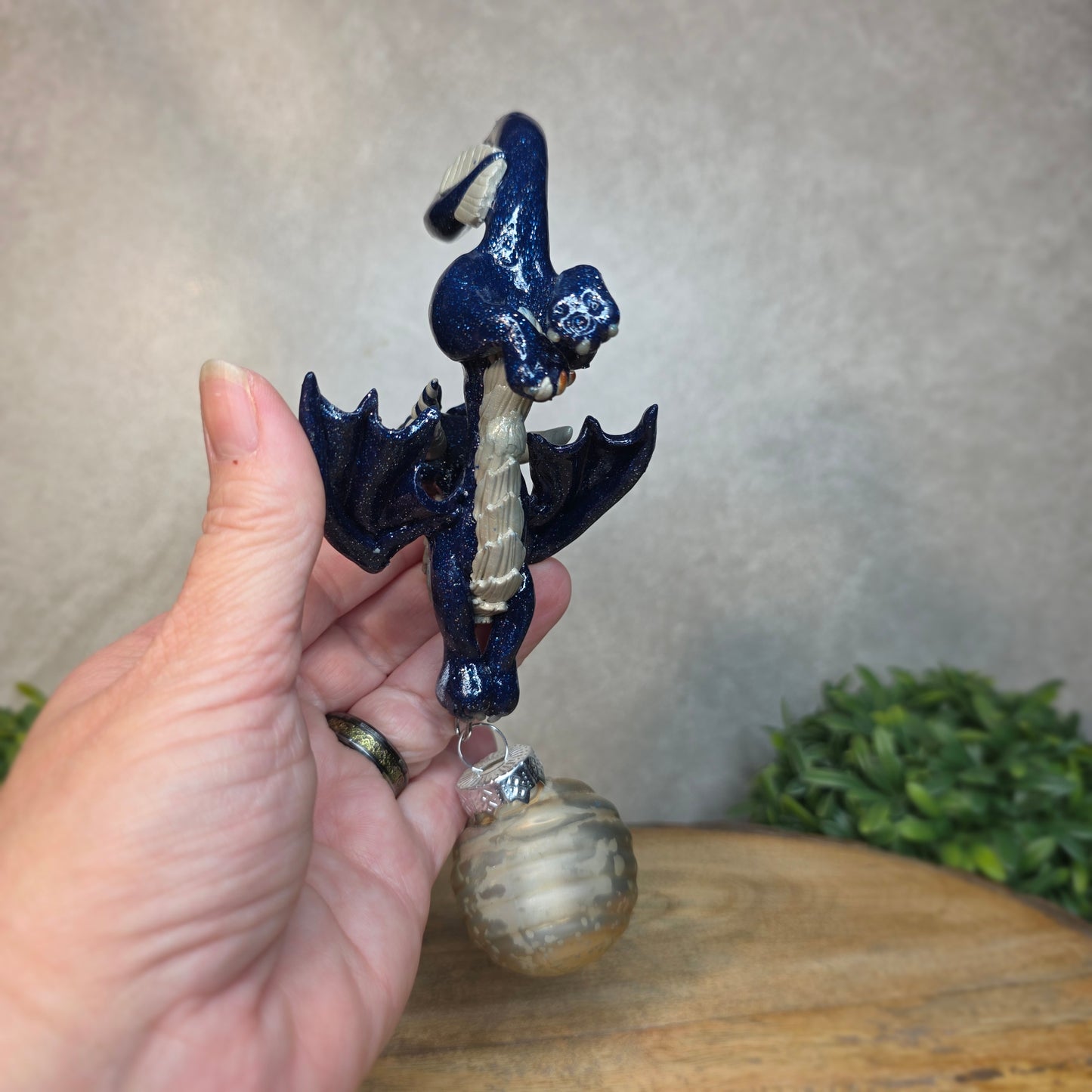 Hand holding a clay dragon with glass ornament against a blurred background