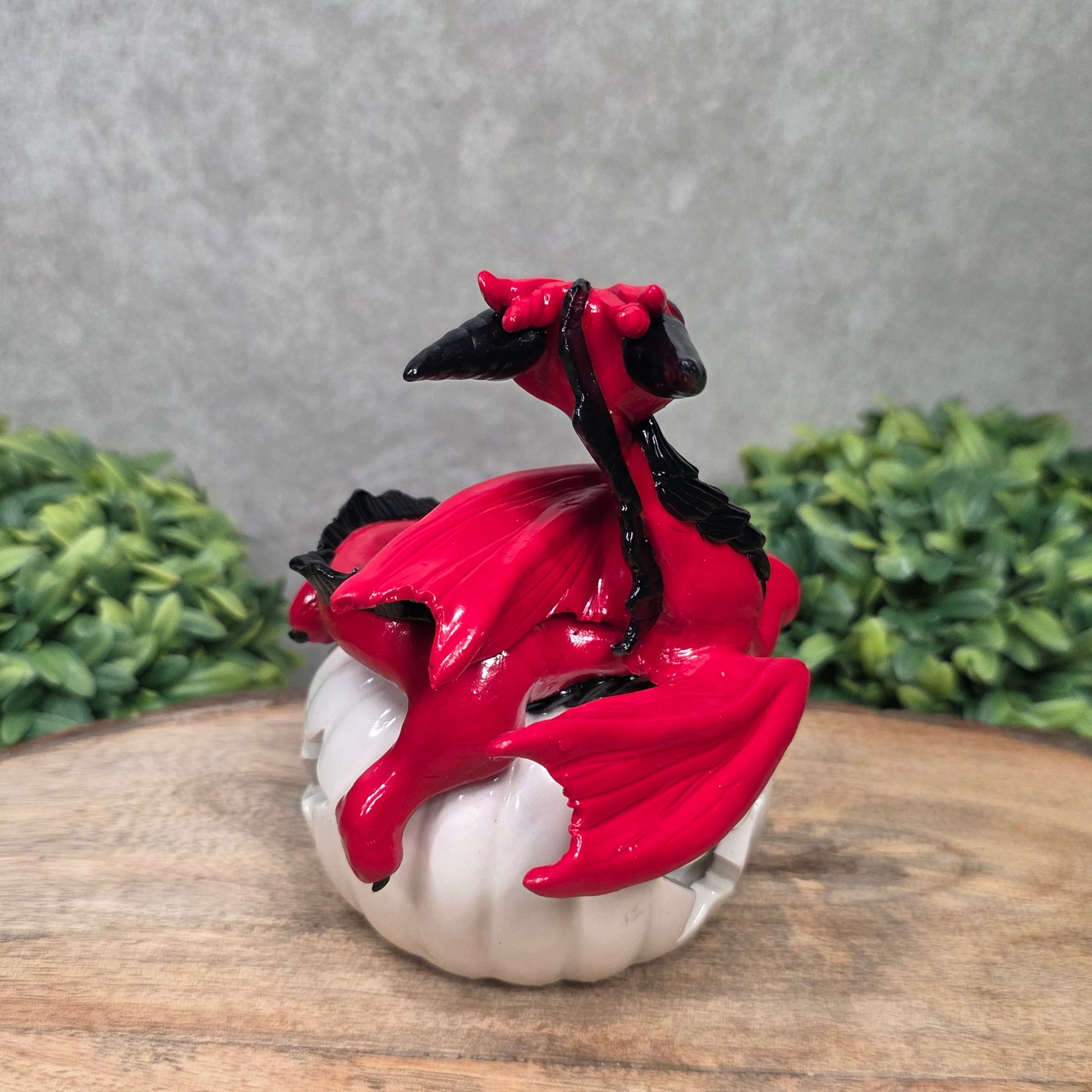 A red dragon sculpture on a white jack o lantern with greenery