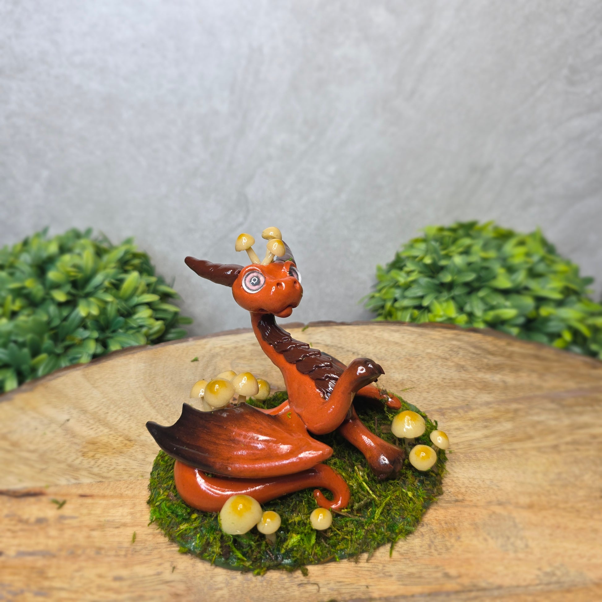 Clay dragon surrounded by mushrooms and moss against a wood background