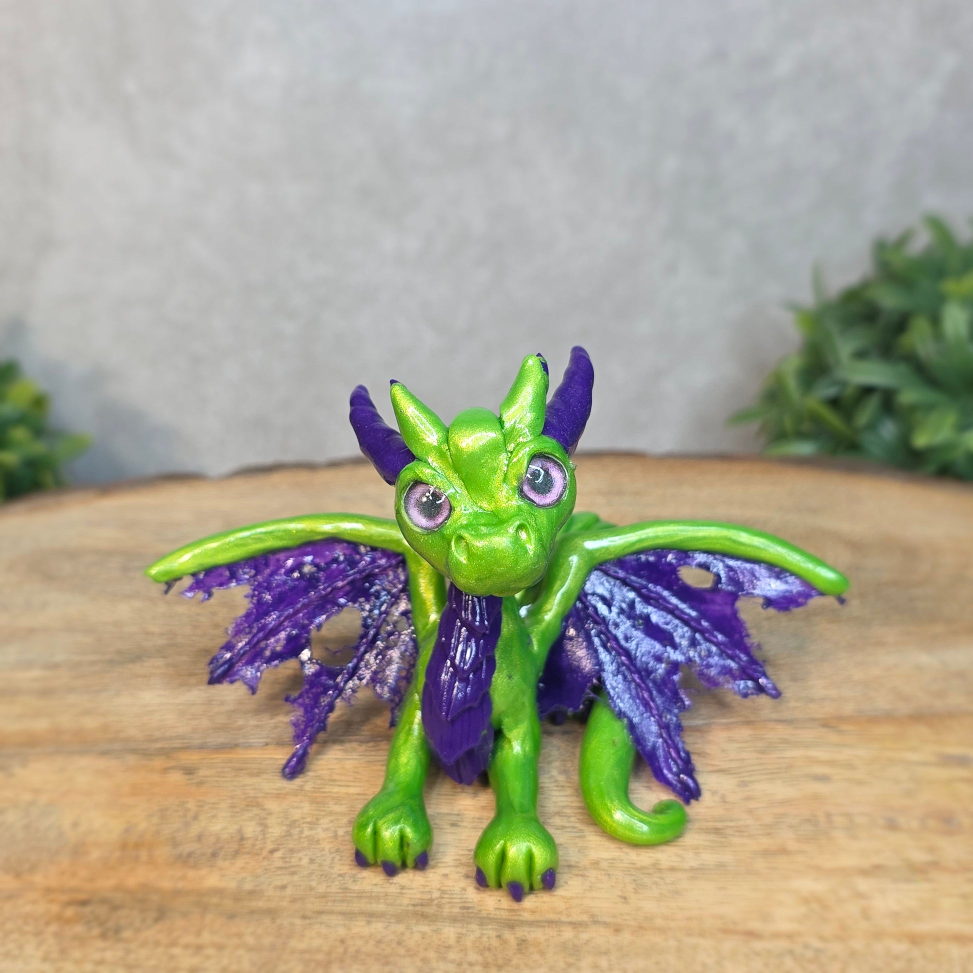 A green and purple clay dragon against a blurred wood surface
