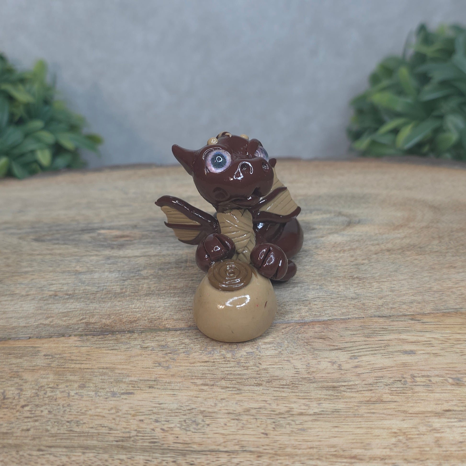 A baby polymer clay dragon with a chocolate truffle against a blurred background