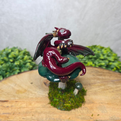 Small dragon figurine on a wooden surface with greenery