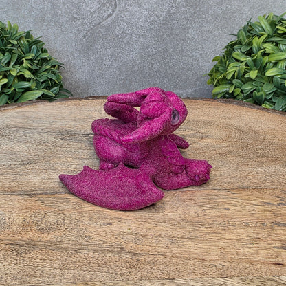 A flocked clay dragon sculpture on a wood surface with greenery.