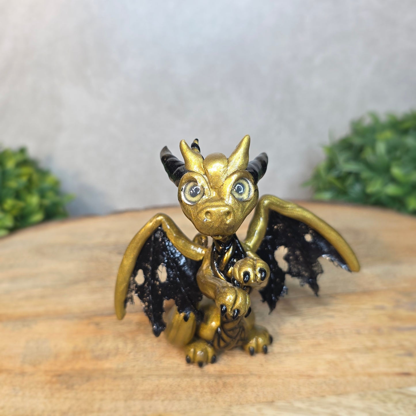 A clay dragon figurine on a wooden surface with a blurred green plant in the background