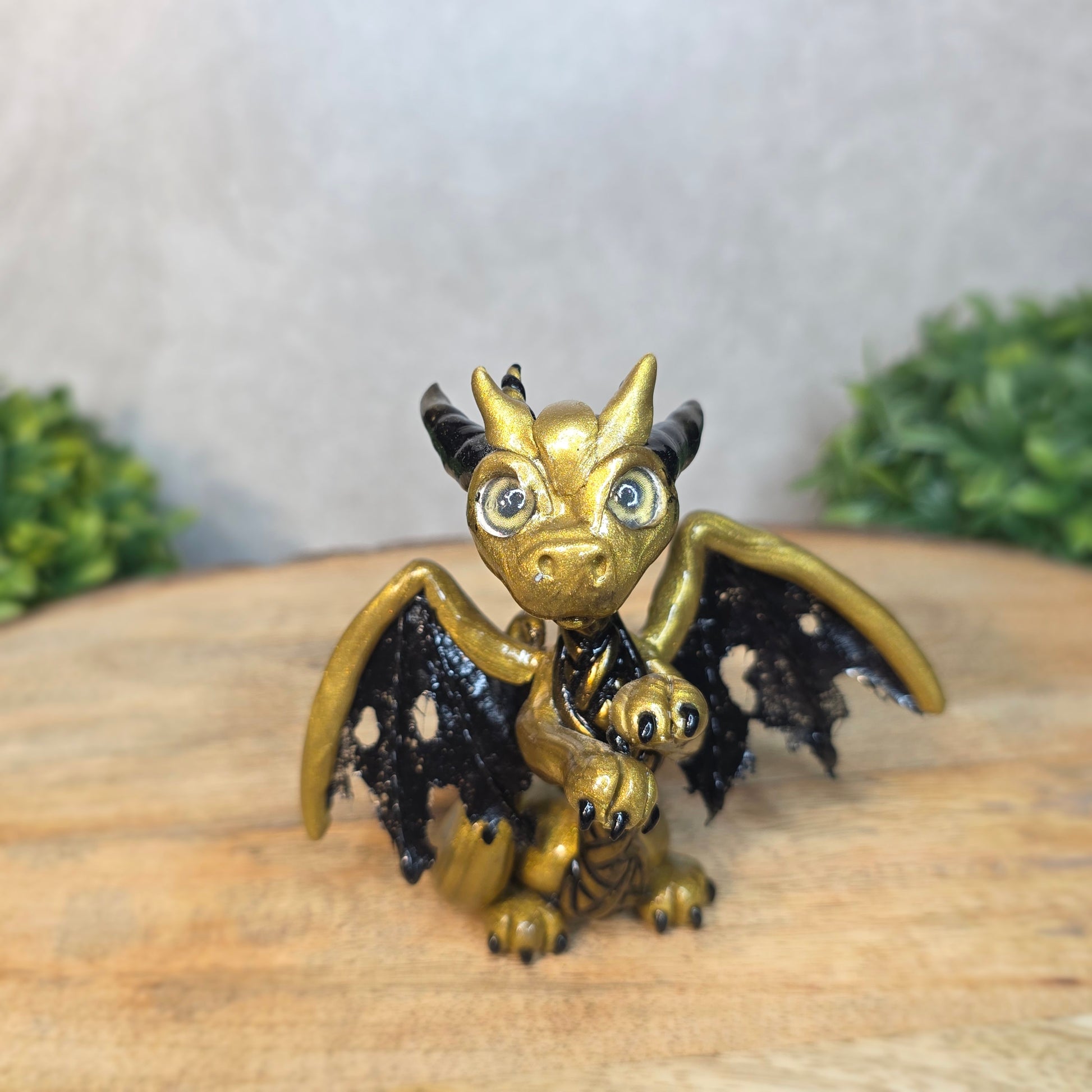 A clay dragon figurine on a wooden surface with a blurred green plant in the background