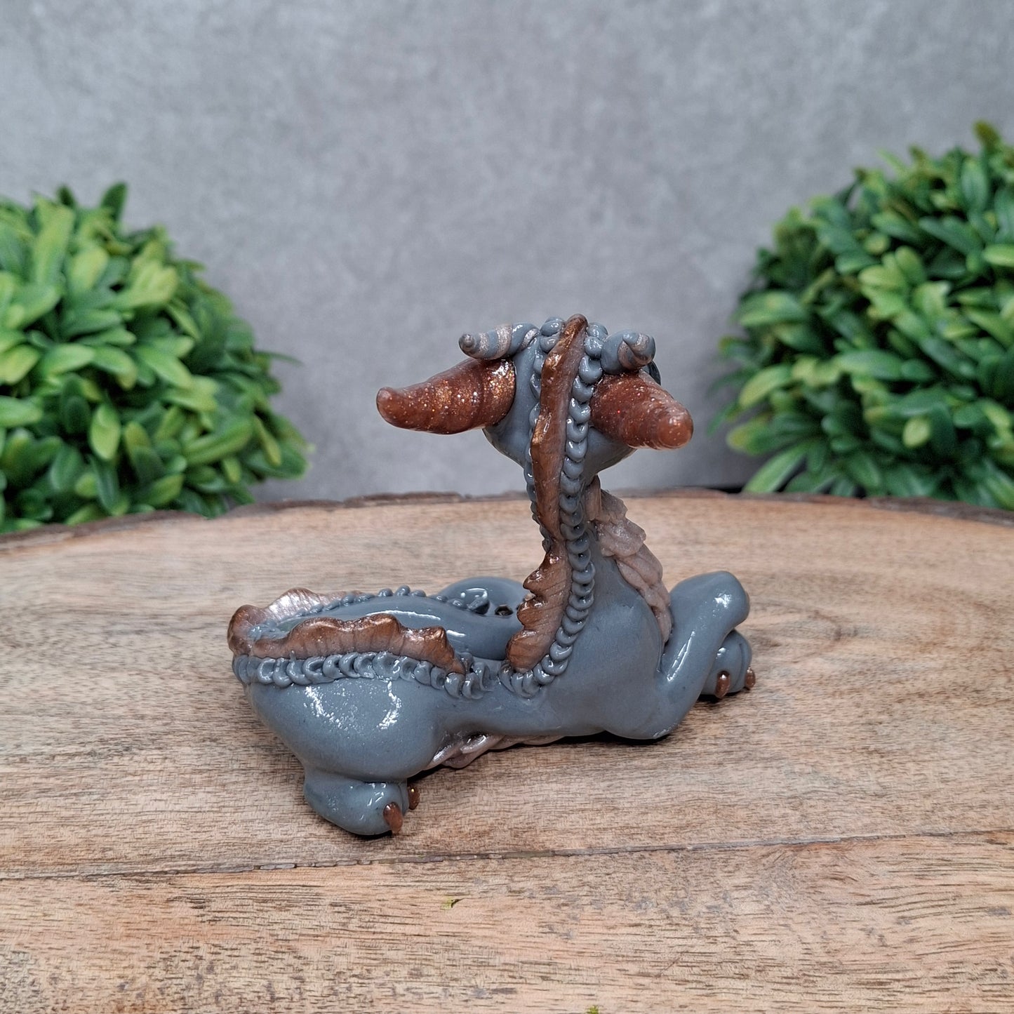 A clay dragon against a wood background with greenery