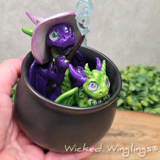 A hand holding a pair of clay dragons in a cauldron