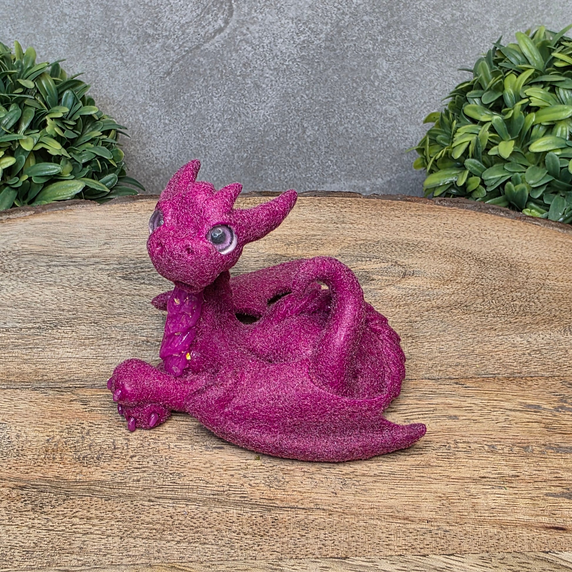 A flocked clay dragon sculpture on a wood surface with greenery.
