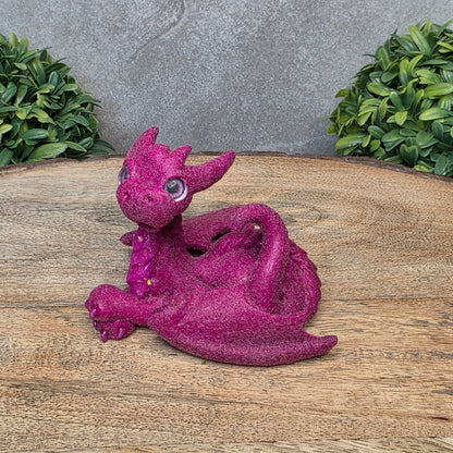 A flocked clay dragon sculpture on a wood surface with greenery.